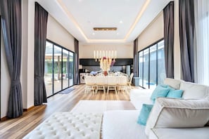 A spacious living area with a large white sofa, a dining table with chairs, and a modern chandelier. - Orange Private Pool Villa, Near Cham Am Beach (Cha-am)