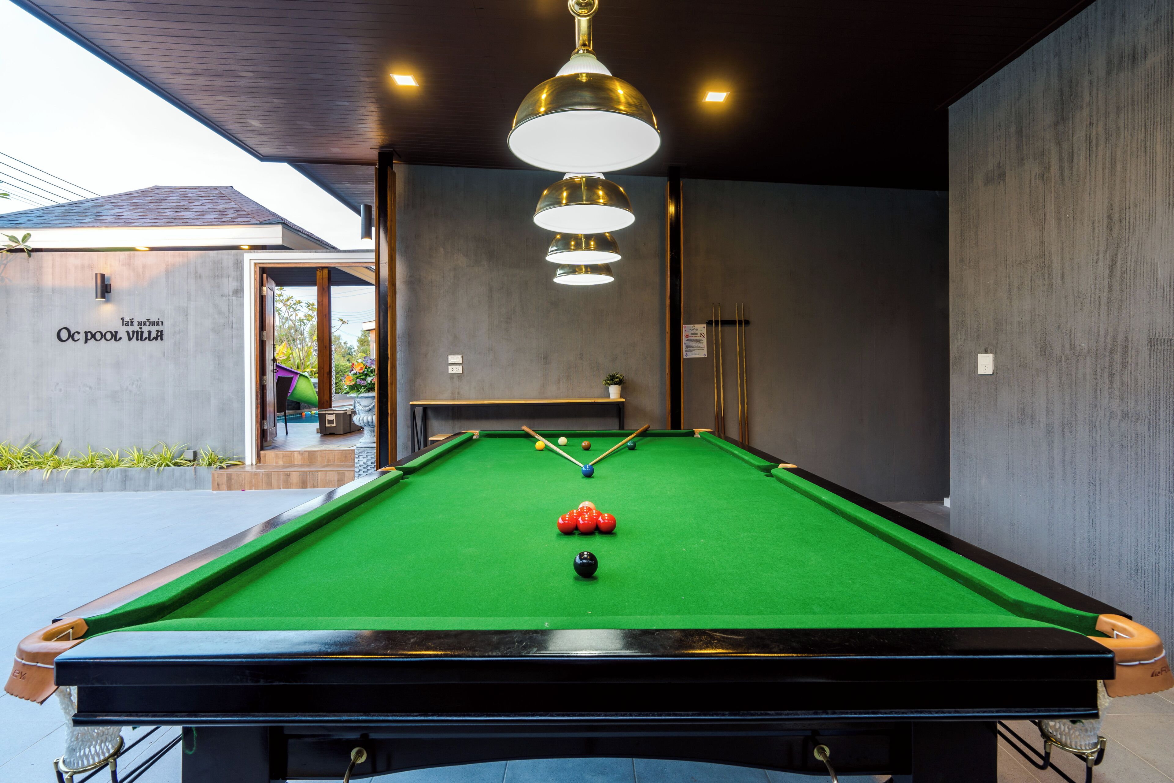 Une table de billard avec des billes, une queue de billard et un luminaire suspendu.