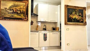 A hotel room with a bed, a chandelier, a kitchen area, and two framed paintings on the walls. - Rome Boulevard Suite - In the heart of Rome, just minutes from St. Peter's Square, (Roma)