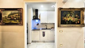 A narrow hallway leading to a kitchen with white cabinets, a black range hood, and a blue kettle. Two framed paintings are on the walls. - Rome Boulevard Suite - In the heart of Rome, just minutes from St. Peter's Square, (Roma)