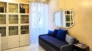 A living room with a chandelier, a sofa with blue cushions, a mirrored wall, and a glass cabinet with books and decorative items. - Rome Boulevard Suite - In the heart of Rome, just minutes from St. Peter's Square, (Roma)