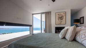A bedroom with a large bed, a view of the sea, a sliding glass door, and a fireplace. - Villa Wellmina - Stunning Sunsets & Relaxing Poolside Vibes! (La Paz)