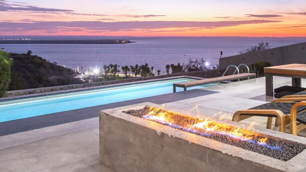 A swimming pool with a fire feature, lounge chairs, and a view of the ocean at sunset. - Villa Wellmina - Stunning Sunsets & Relaxing Poolside Vibes! (La Paz)