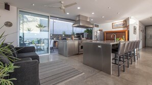 A modern kitchen with a large island, a dining area with chairs, and a view through a glass door. - Villa Wellmina - Stunning Sunsets & Relaxing Poolside Vibes! (La Paz)