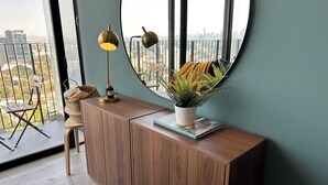 Una sala de estar moderna con un espejo redondo grande, un mueble de madera, una helecho en maceta y una mesita con una lámpara y una cesta.