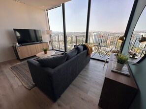 Un soggiorno moderno con un divano grande, una televisione e un balcone con vista sulla città.