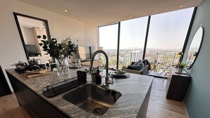 Cocina moderna con una isla grande, pileta de acero inoxidable y vista a la ciudad a través de amplios ventanales.