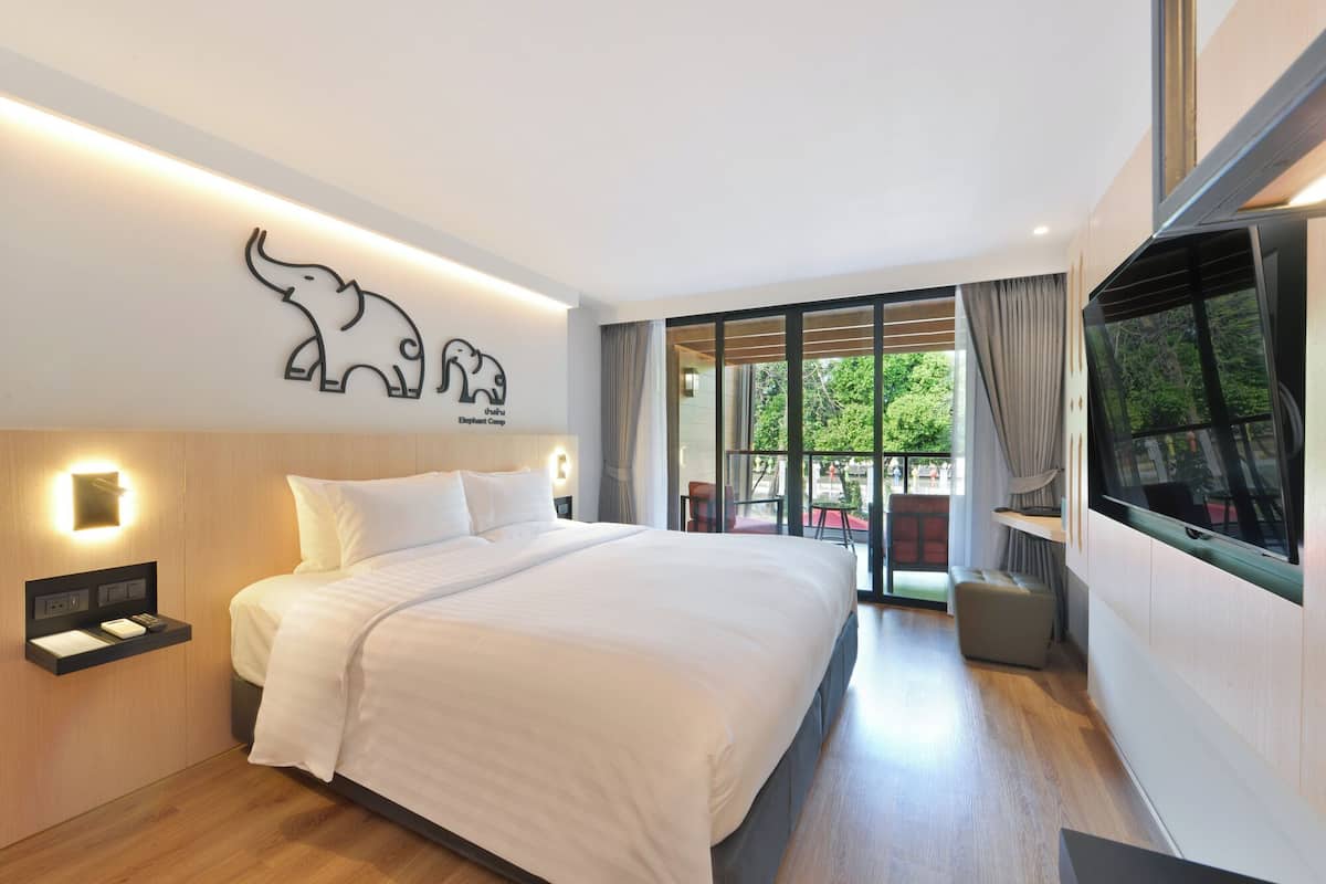 Habitación de hotel moderna con una cama grande, una obra de arte con un elefante colgada en la pared, un televisor y un balcón con vistas.