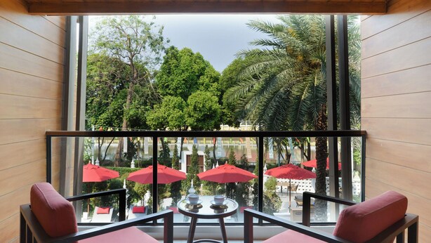 Un balcón con vista a un patio de restaurante, con sombrillas rojas y mesas al aire libre.