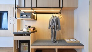 Habitación de hotel compacta con kitchenette, un refrigerador pequeño, una zona de estar con un banco y un perchero.