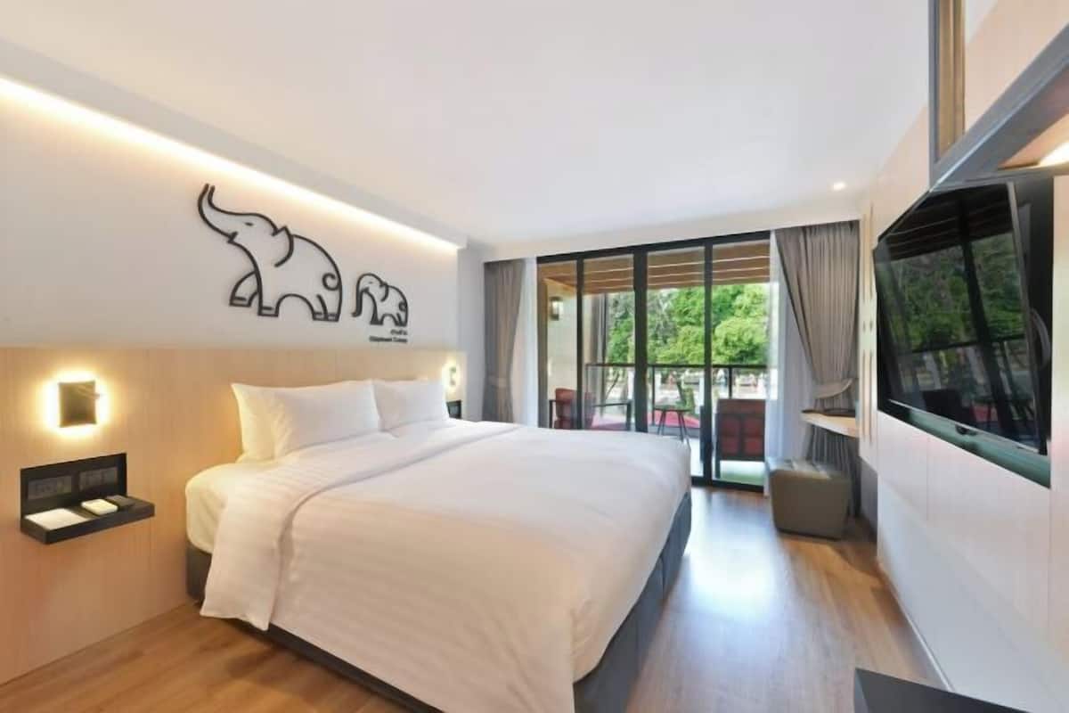 Una habitación de hotel moderna con una cama grande, un adorno de elefante en la pared, un televisor y un divisor de vidrio corredizo que da a un espacio al aire libre.