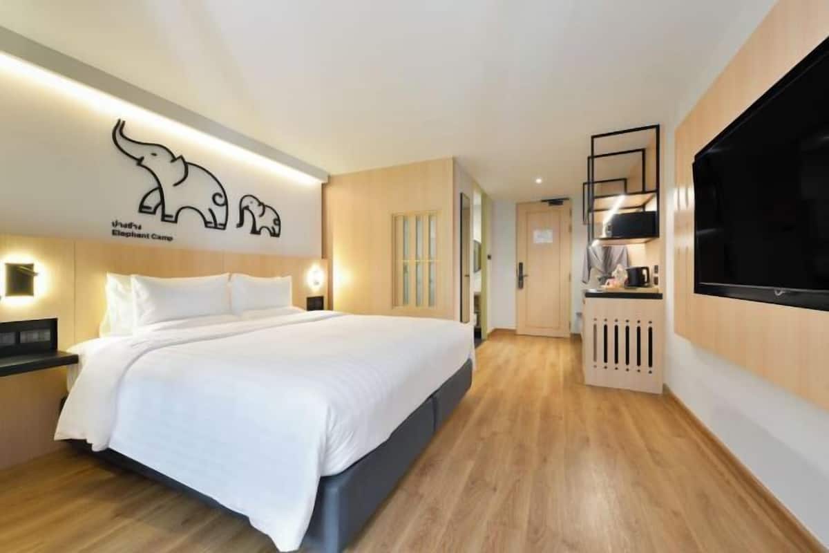Una habitación de hotel con cama, mesitas de noche, un televisor montado en la pared y una zona de cocina.