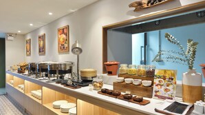 Un montaje tipo buffet con diversas opciones de comida y utensilios, una máquina de café y elementos decorativos como cuadros y una planta.