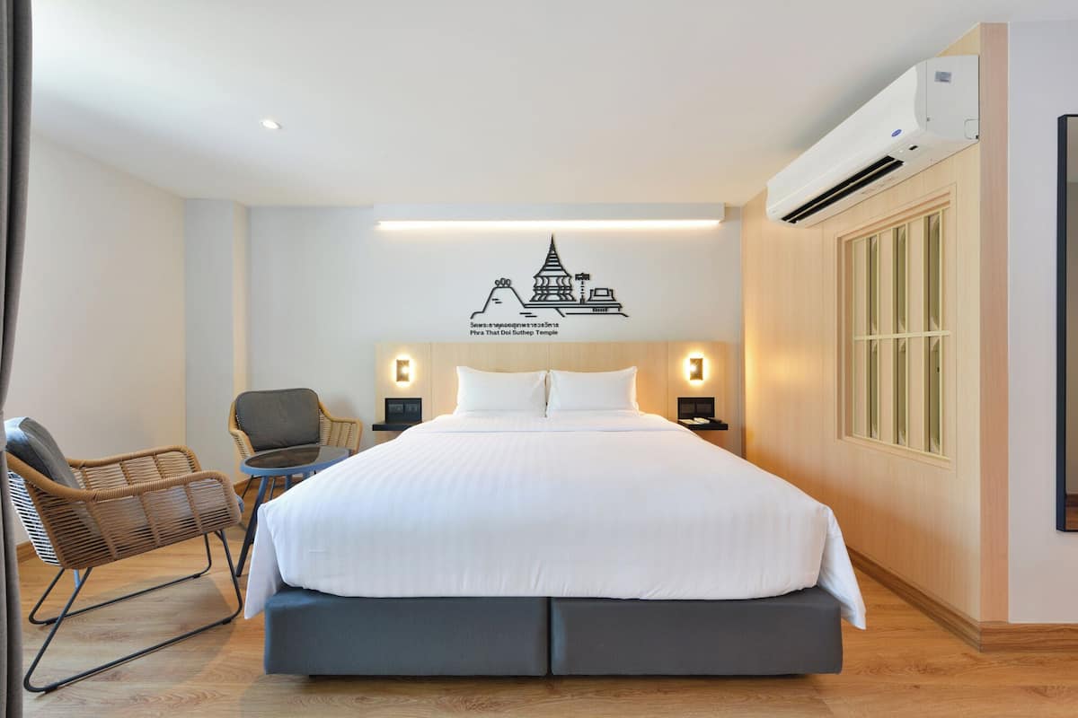 Una habitación de hotel con una cama, una silla, un escritorio y un aire acondicionado.