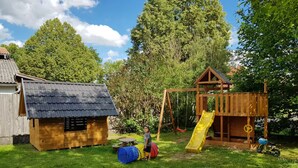 A wooden playhouse with a slide, a small shed, and a blue ball pit in a grassy yard. - Modern 2-room attic apartment in the heart of the Rhön (Ostheim vor der Rhön)