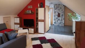A living room with a red wall, a television, and a small white table. - Modern 2-room attic apartment in the heart of the Rhön (Ostheim vor der Rhön)