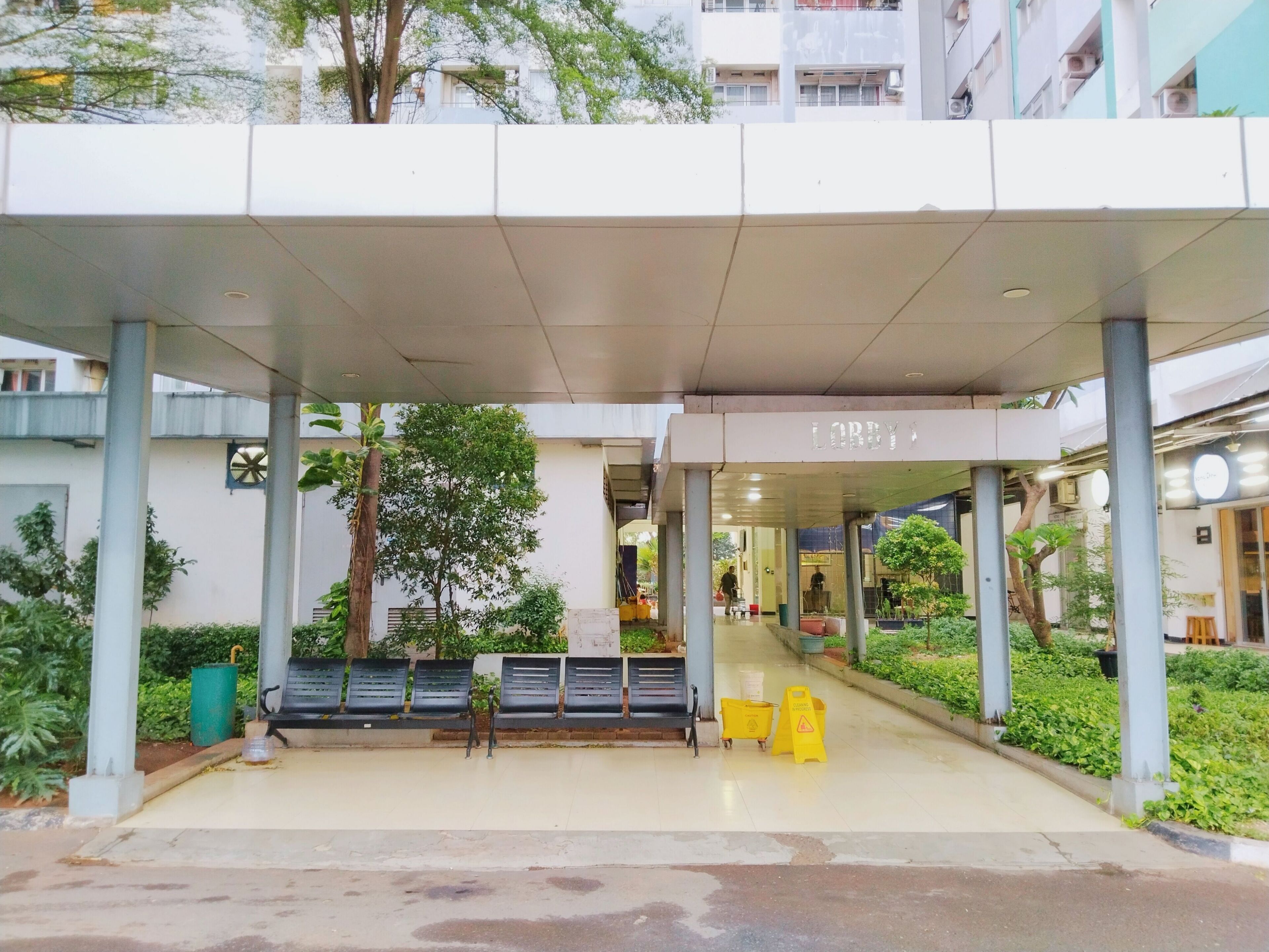 A covered entrance with a 'Lobby' sign, outdoor seating, and greenery.