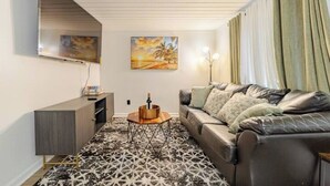 A living room with a sofa, a coffee table, a TV mounted on the wall, and a painting.