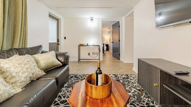 A modern living room with a leather sofa, a wooden coffee table with a bottle, and a patterned rug.