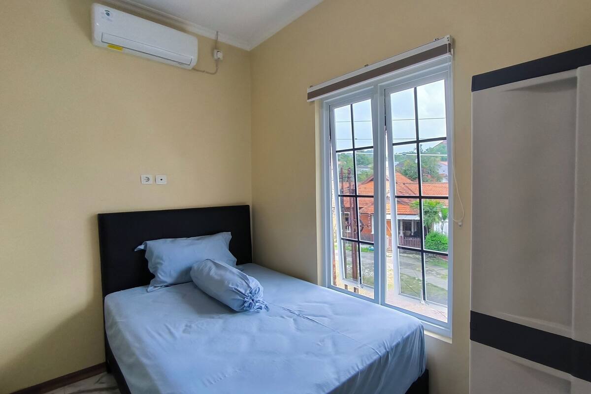 A bedroom with a bed, a window, and an air conditioning unit.