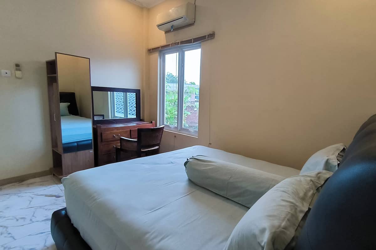 A bedroom with a bed, a desk with a chair, a window, and an air conditioning unit.