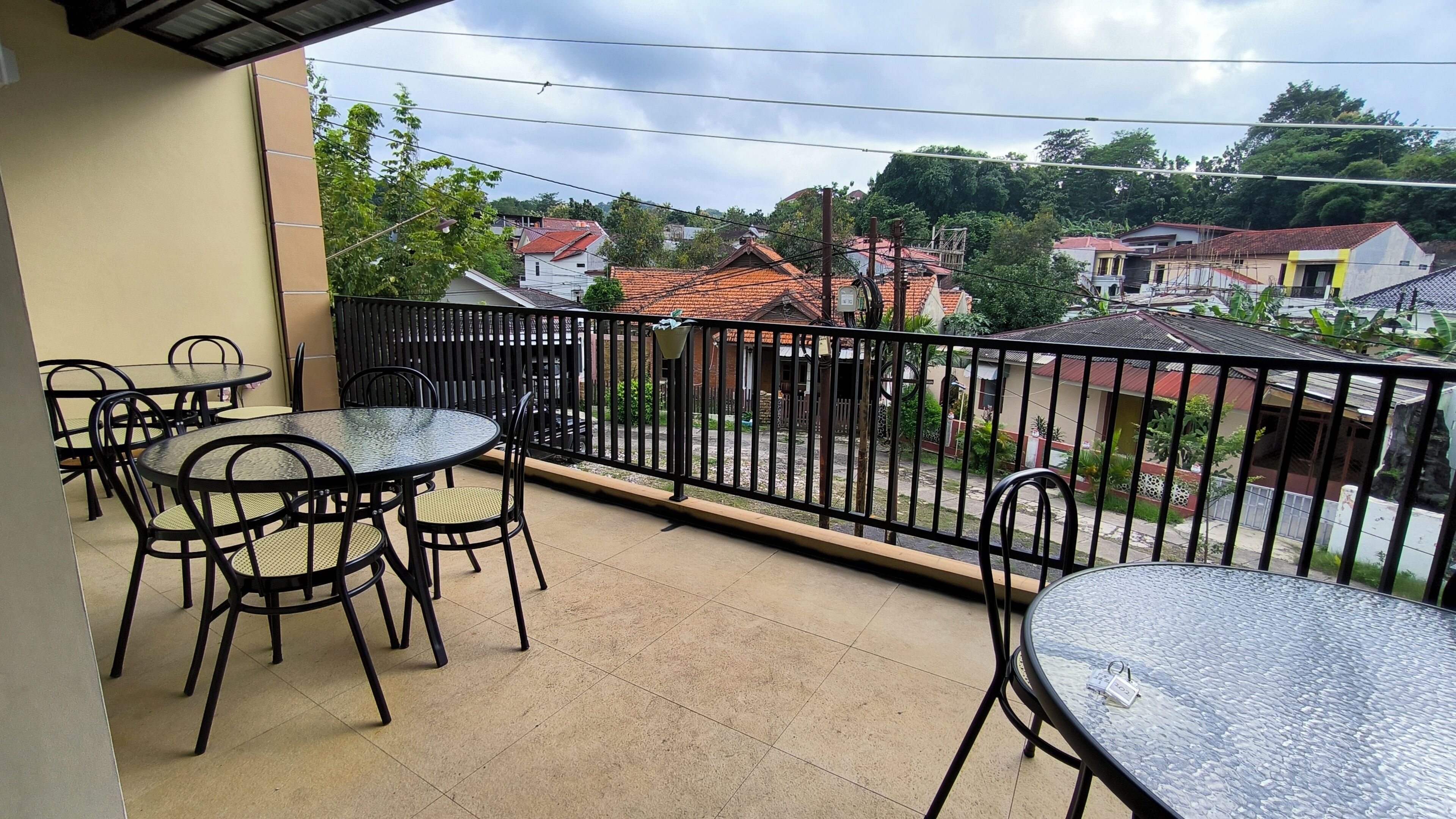 A balcony with a view of houses, a tiled floor, and metal chairs.