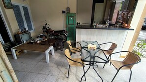 Ein kleiner, gemütlicher Außenbereich mit Holztisch und -stühlen, einem Fernseher und einer grünen Tür.