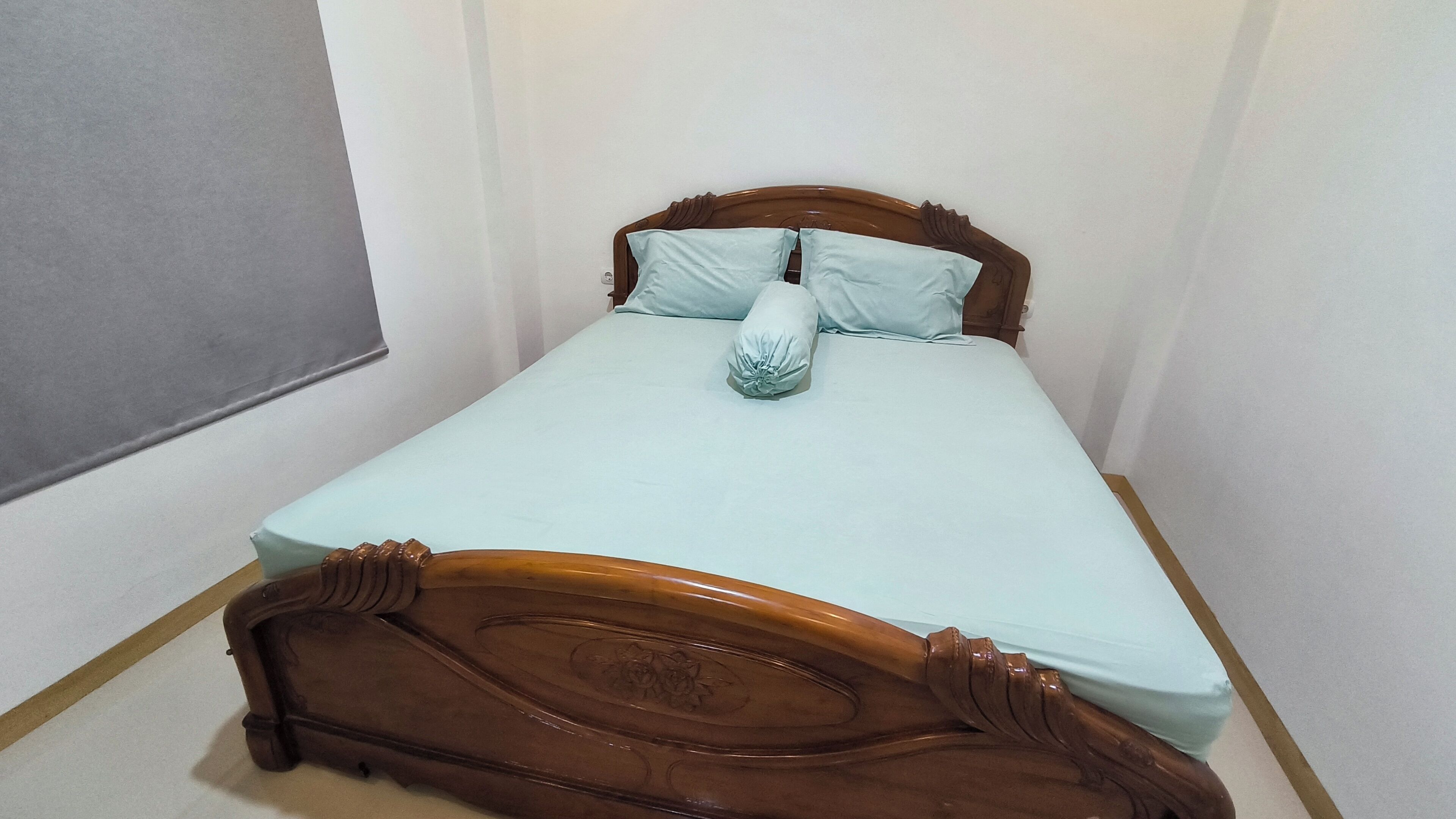 A small, neatly made bed with a wooden headboard and light blue bedding.