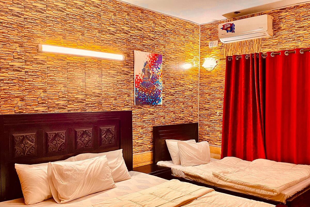 A hotel room with two beds, a decorative wall, an air conditioning unit, and a red curtain.