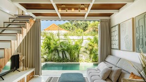 A modern living room with a pool view, a staircase, and a sofa. - Tropical 1BR Private Pool Villa, 8 mins to beach In Uluwatu (Pecatu)