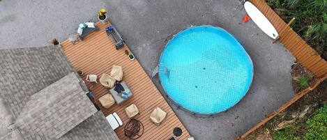 Vista aérea de un patio trasero con piscina, terraza de madera y mobiliario exterior.