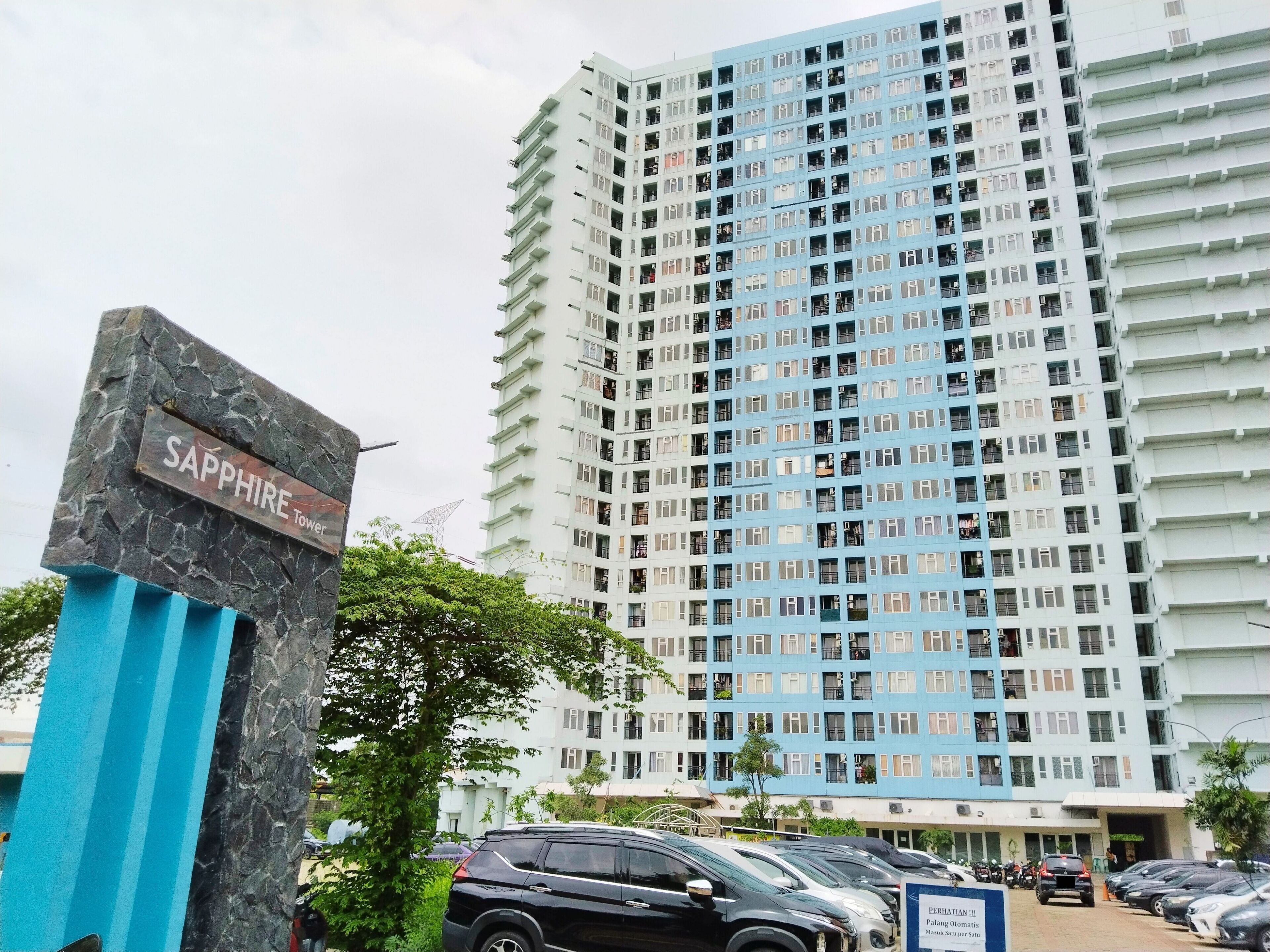 Ein hohes Wohngebäude namens 'Sapphire Tower' mit mehreren Balkonen und einem Schild, das 'Palace Hotel' anzeigt, mit Annehmlichkeiten wie einem Spa und einem Restaurant.