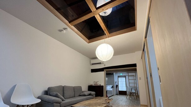 Una sala moderna con techo de madera, sofás grises, una mesa de centro de madera y una lámpara colgante blanca.