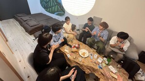 Un grupo de personas sentadas alrededor de una mesa en una habitación moderna con un mural en la pared y una lámpara colgante grande.