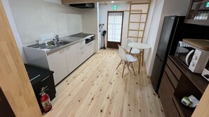 Cocina compacta con pileta, estufa y microondas. Hay un pequeño comedor con una mesa y sillas. Se observa un extintor en el piso.