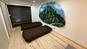 Una habitación con piso de madera, un mural de montañas y dos camas de color oscuro.