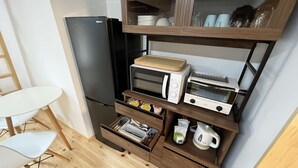 Una cocina compacta con un refrigerador negro, un microondas, un tostador y un mueble de madera con puertas de vidrio.