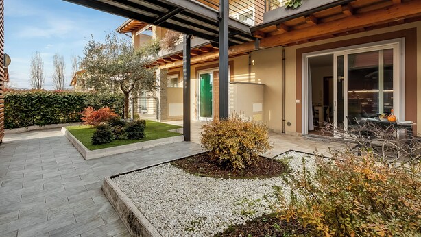 A modern building with a covered outdoor area, a green door, and a patio with a table and chairs. - Residence Due Laghi (Ispra)