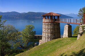 A stone tower with a red roof overlooking a lake, surrounded by greenery and mountains. - Residence Due Laghi (Ispra)