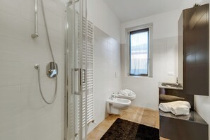 A modern bathroom with a glass shower enclosure, a bidet, a sink with a mirror, and a window providing natural light. - Residence Due Laghi (Ispra)