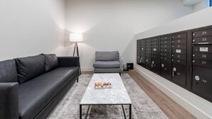 A modern living room with a black leather sofa, a grey sofa, a marble coffee table, and a floor lamp. There are black mailboxes on the right wall. - Pleasant Condotel with WiFi in Vibrant First Hill (Seattle)