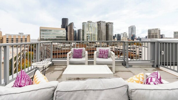 A rooftop terrace with a white sofa set, a small table, and colorful cushions. A city skyline is visible in the background. - Pleasant Condotel with WiFi in Vibrant First Hill (Seattle)