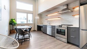 A modern kitchen with stainless steel appliances, a dining area with a white chair, and large windows providing natural light. - Pleasant Condotel with WiFi in Vibrant First Hill (Seattle)