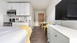 A compact hotel room with a kitchenette, a bed with a yellow throw, a dining area with a table and chairs, and a TV mounted on the wall. - Pleasant Condotel with WiFi in Vibrant First Hill (Seattle)