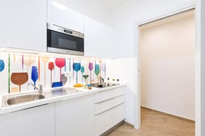Una cocina moderna con armarios blancos, un lavamanos de acero inoxidable y un horno empotrado.