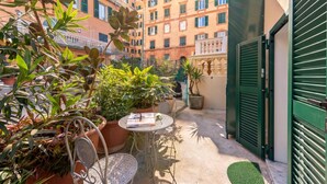 Un patio con plantas en macetas, una mesa de metal con sillas y una verja verde.
