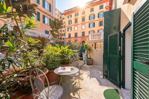 A courtyard with potted plants, a metal table with chairs, and a green gate. - Central Flat In Genova (Genoa)