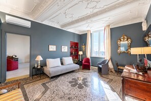 A room with a grey sofa, red armchair, and a wooden desk with a lamp. - Precious House Genova Porto Antico (Genoa)