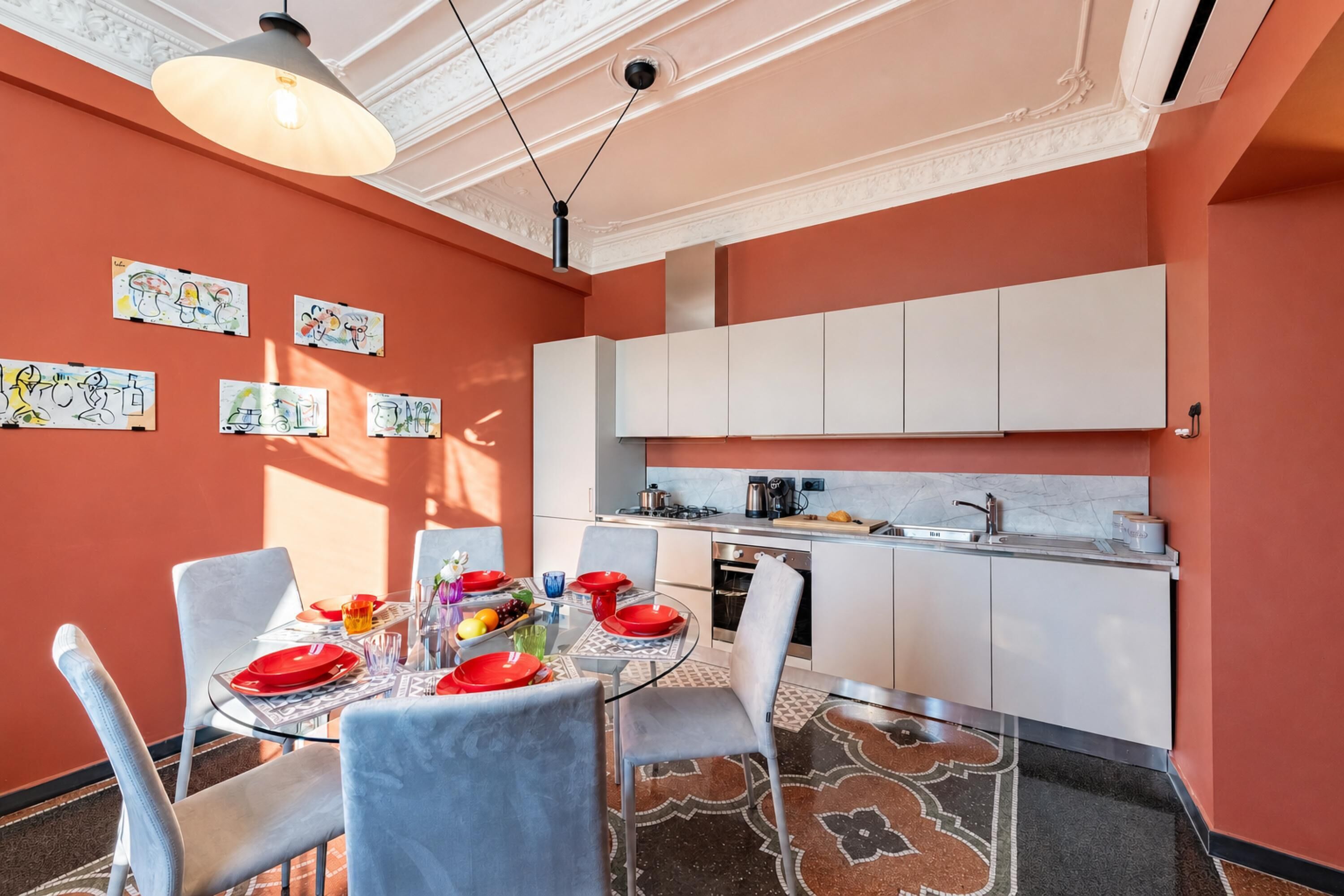A compact kitchen with white cabinets, a dining table set with red plates, and artwork on the walls.
