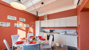 A compact kitchen with white cabinets, a dining table set with red plates, and artwork on the walls. - Precious House Genova Porto Antico (Genoa)